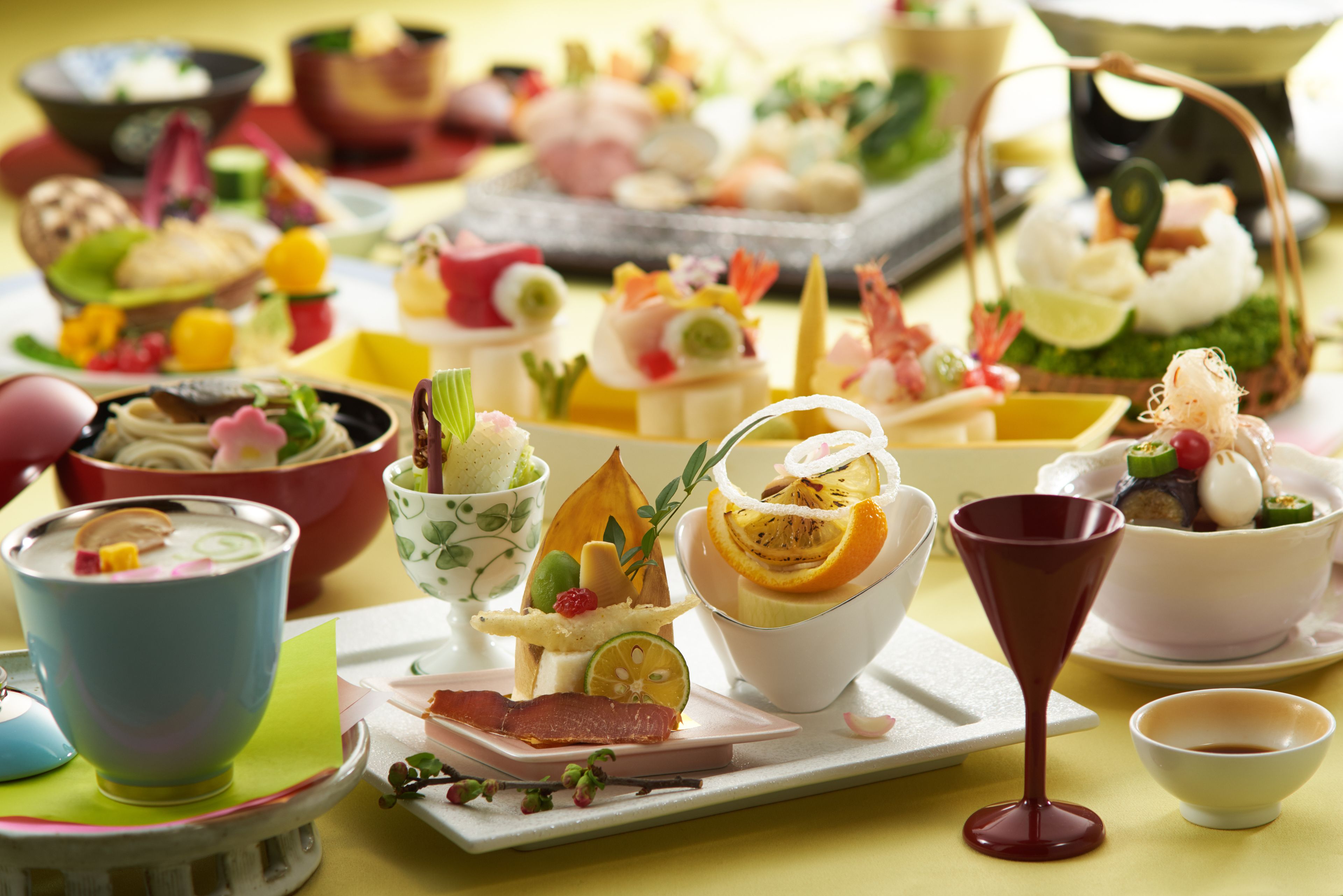 A variety of food and drink items on a table, including bowls, plates, and a wine glass.