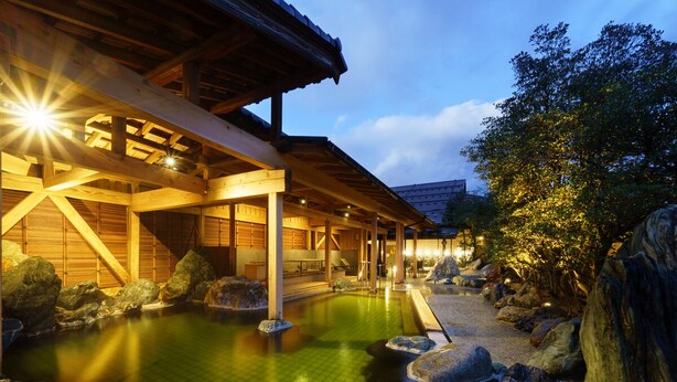 Un onsen japonés tradicional con estructura de madera y un sendero de piedra que conduce al área de aguas termales.