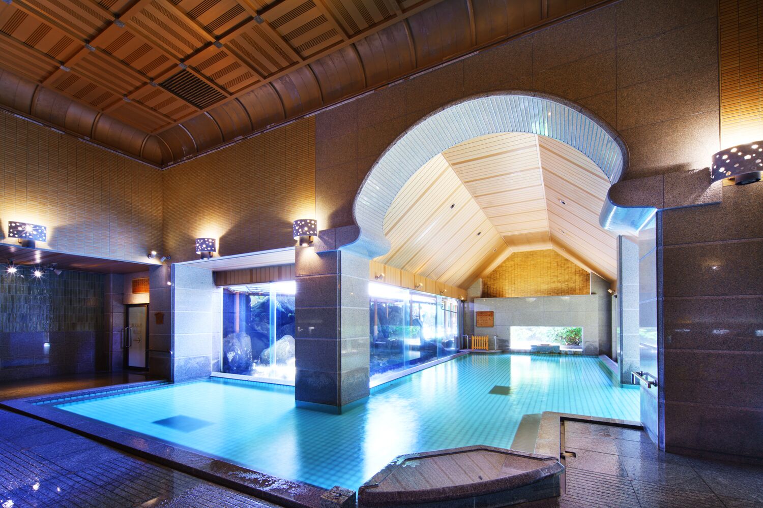 Una amplia piscina interior con techo de madera y paredes de piedra.