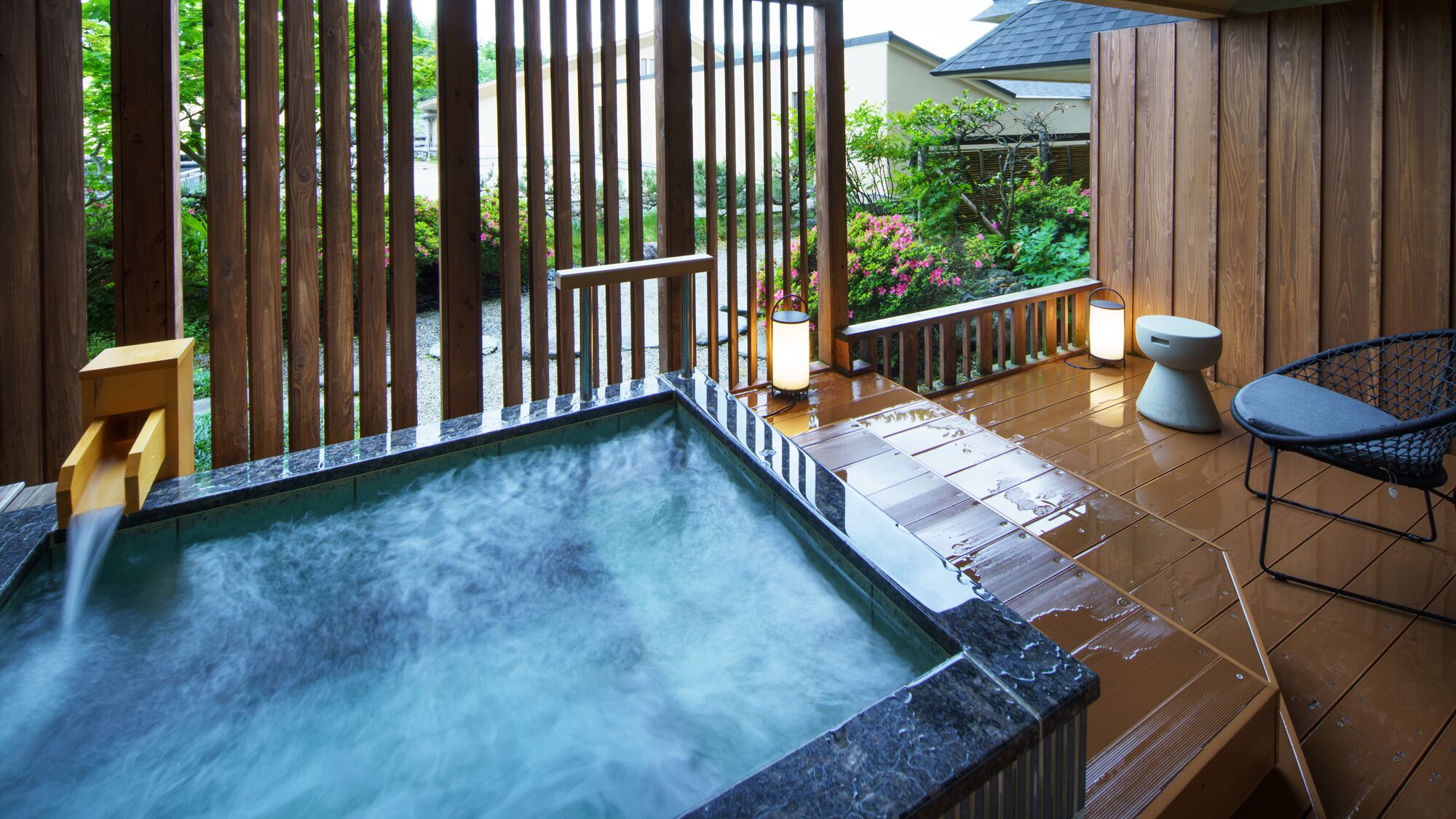 A hot tub with a wooden fence and a chair, surrounded by a garden.