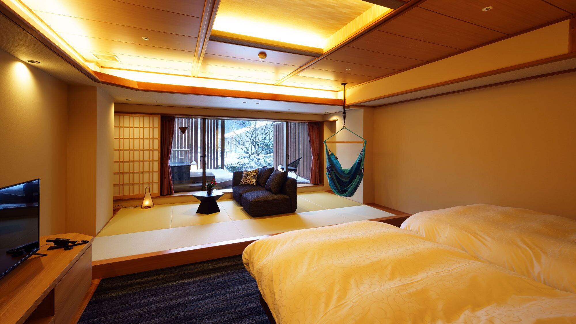 A hotel room with a sofa, two beds, a TV, a desk, and a view of a snowy garden.