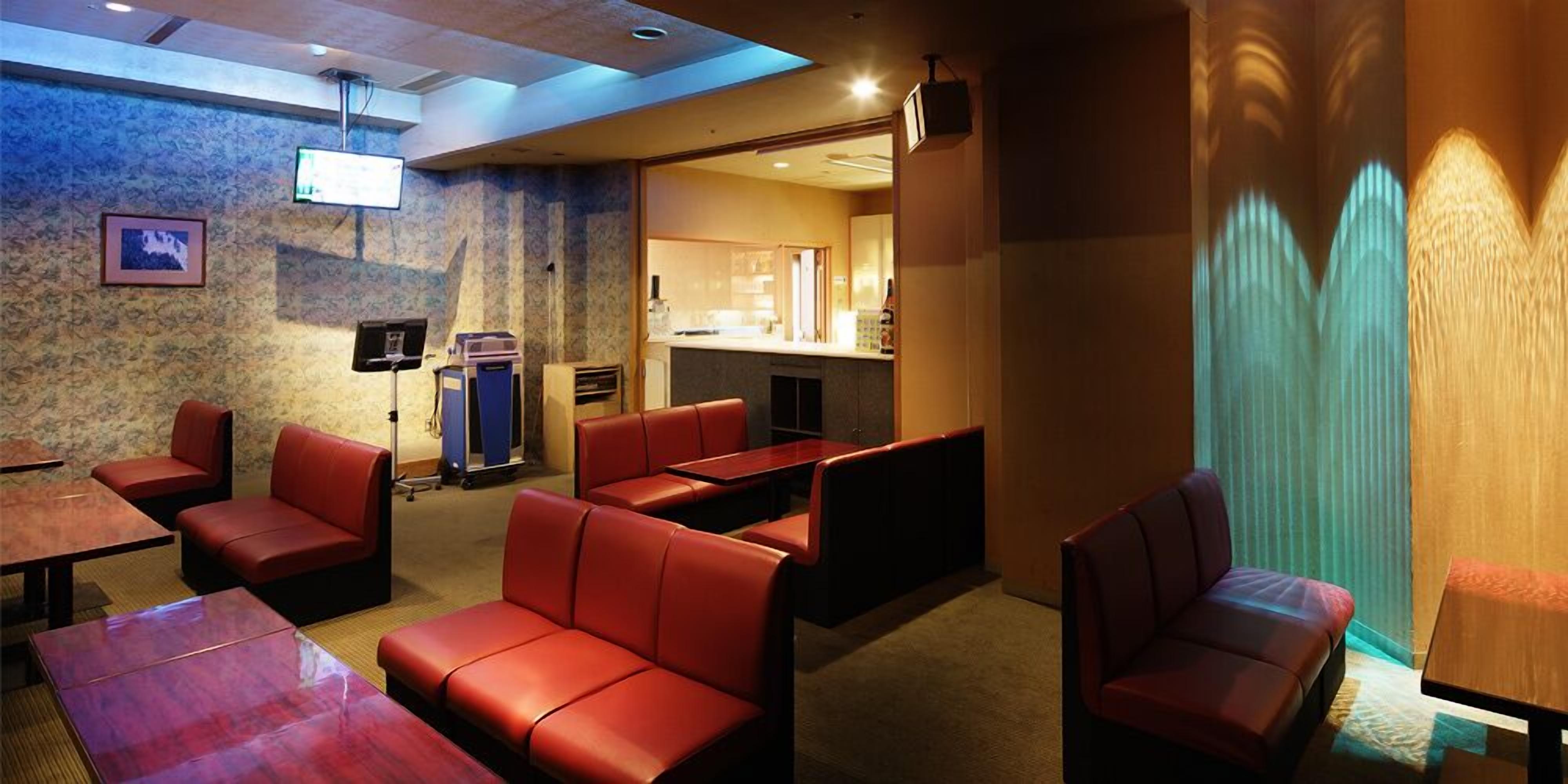 A hotel lobby with red leather seating, a reception desk, and a visible kitchen area.
