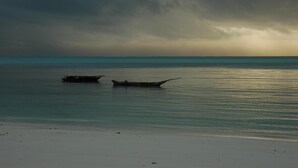 A beach with calm waters and two boats. - Coco Beach Hotel (Jambiani)