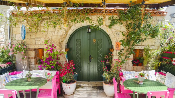 An outdoor seating area with tables and chairs, a green door, and potted plants. - Apaz Alacati Hotel (Cesme)