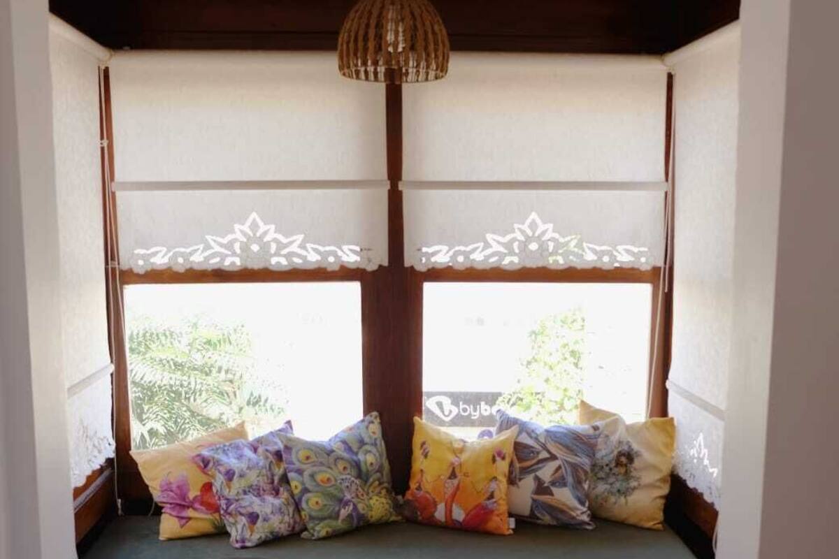 A cozy room with a built-in bench under a window, featuring a woven lamp and patterned cushions.