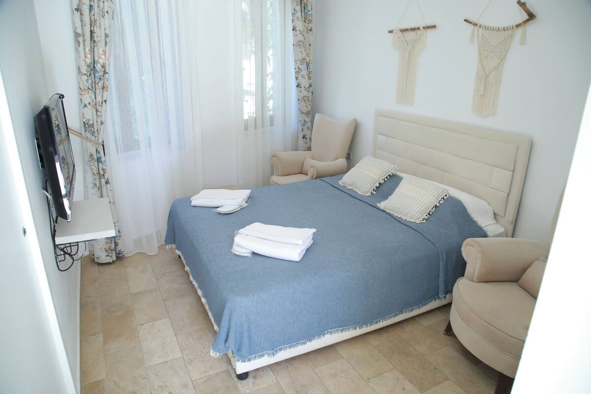 A neatly made bed with a blue bedspread and white towels, a beige armchair, and a television on a stand.