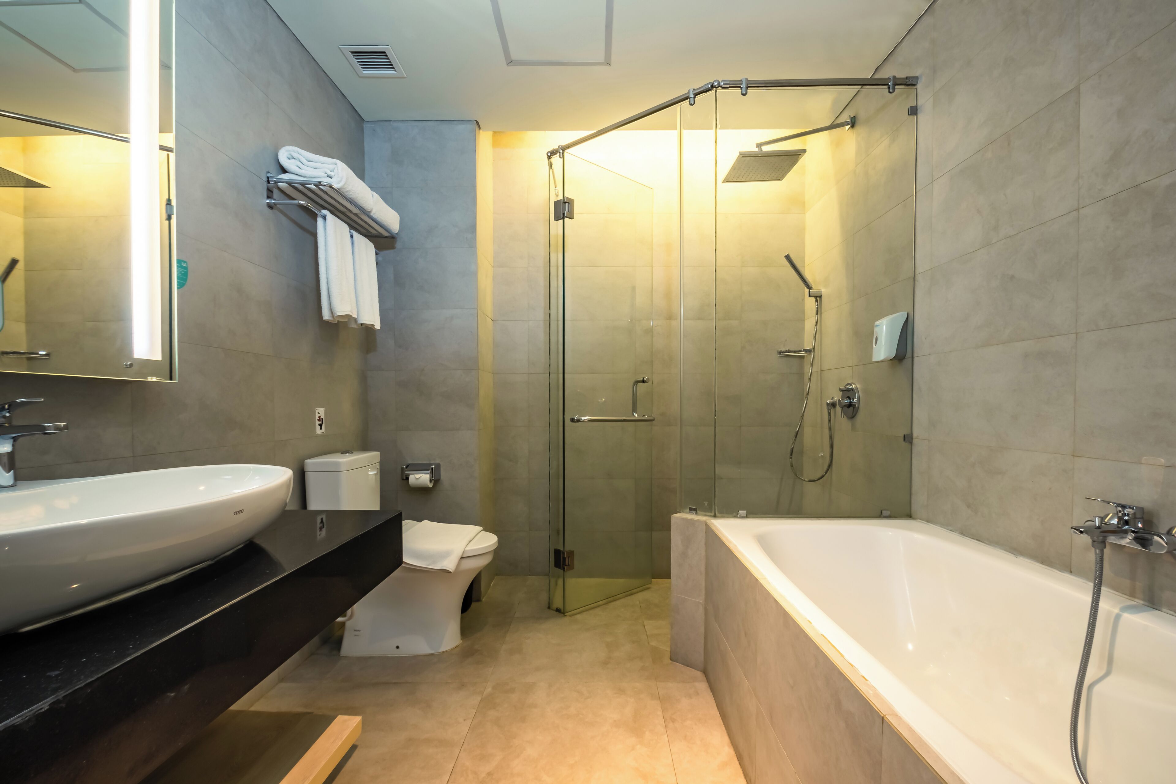 Un baño moderno con una bañera grande, ducha con mampara de vidrio, inodoro y lavabo con espejo.