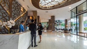 Um hall de hotel moderno com balcões de recepção de mármore, uma parede decorativa e um painel de vidro.