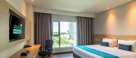 A hotel room with a bed, a desk, a chair, a TV, and a window with curtains.