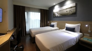 Quarto de hotel com duas camas, uma mesa, uma cadeira, uma televisão e um quadro na parede.