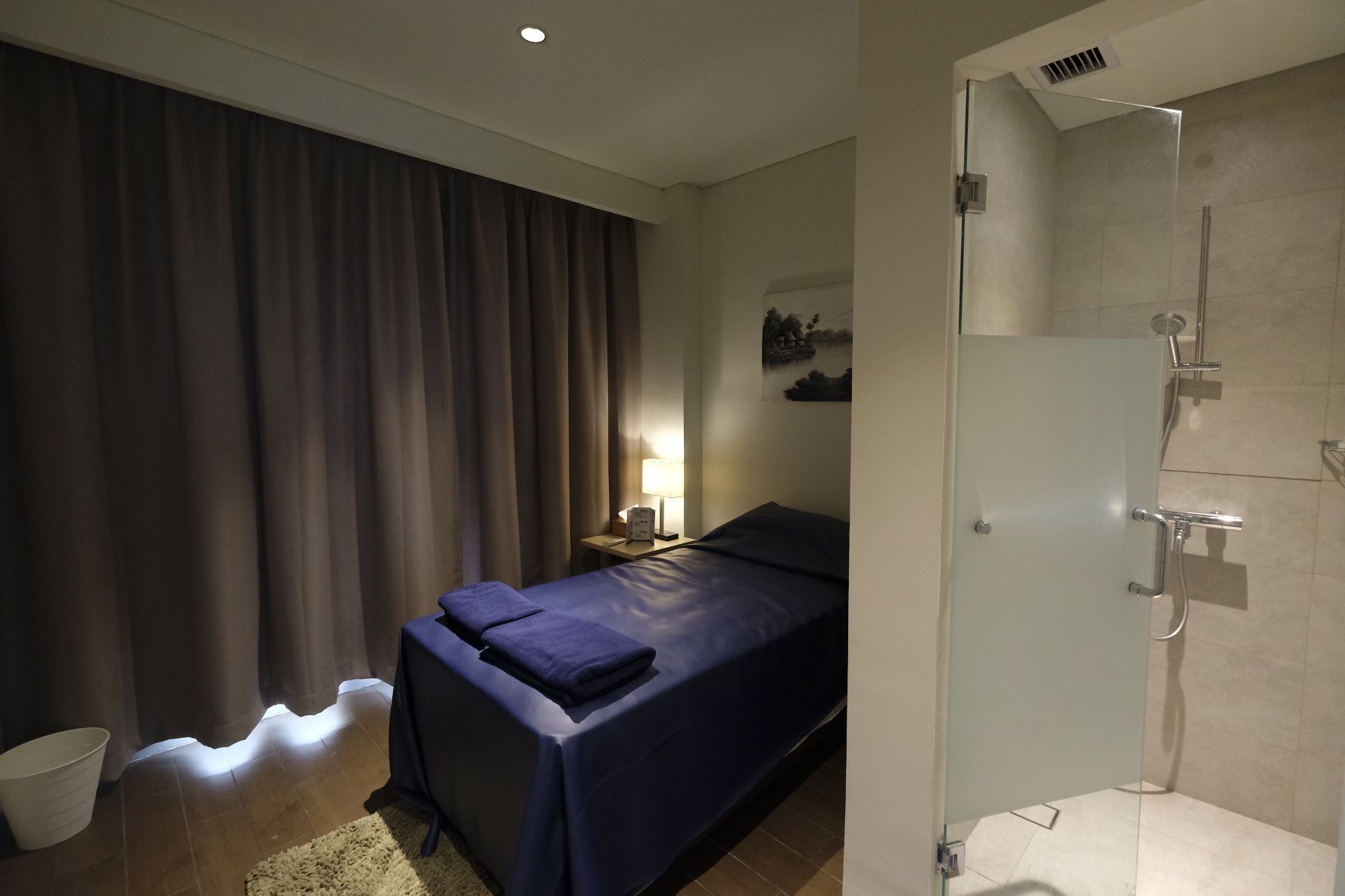 Un dormitorio con cama, mesita de noche, lámpara, ducha y cortina.
