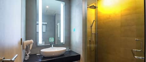 A modern bathroom with a large mirror, a sink, and a glass-enclosed shower.