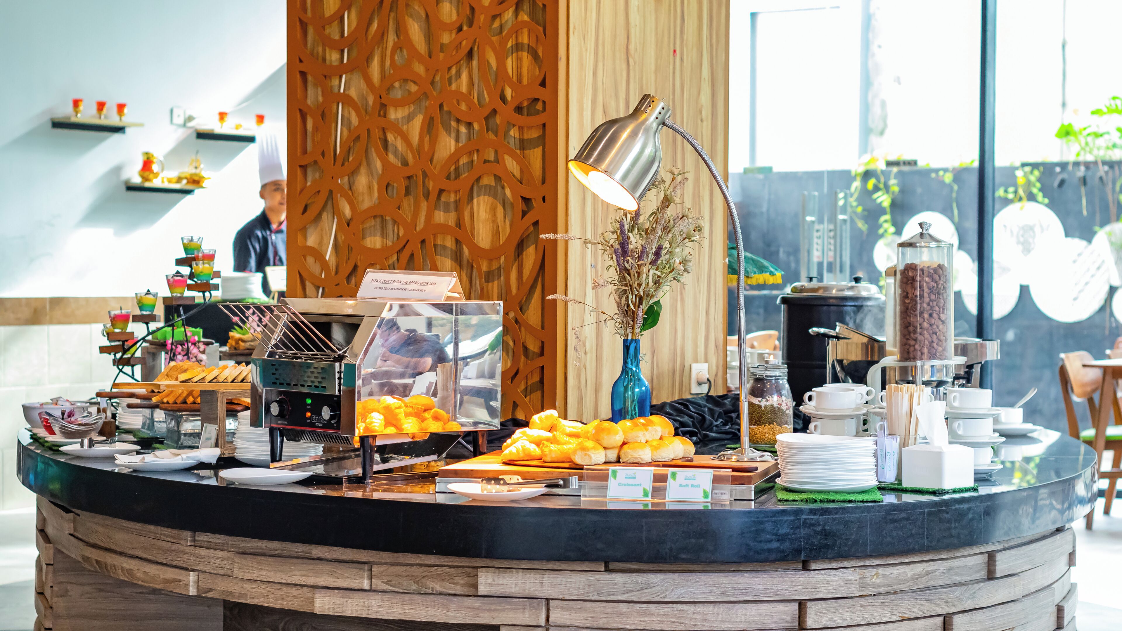 A breakfast buffet with various food items, a coffee station, and a decorative vase with flowers.