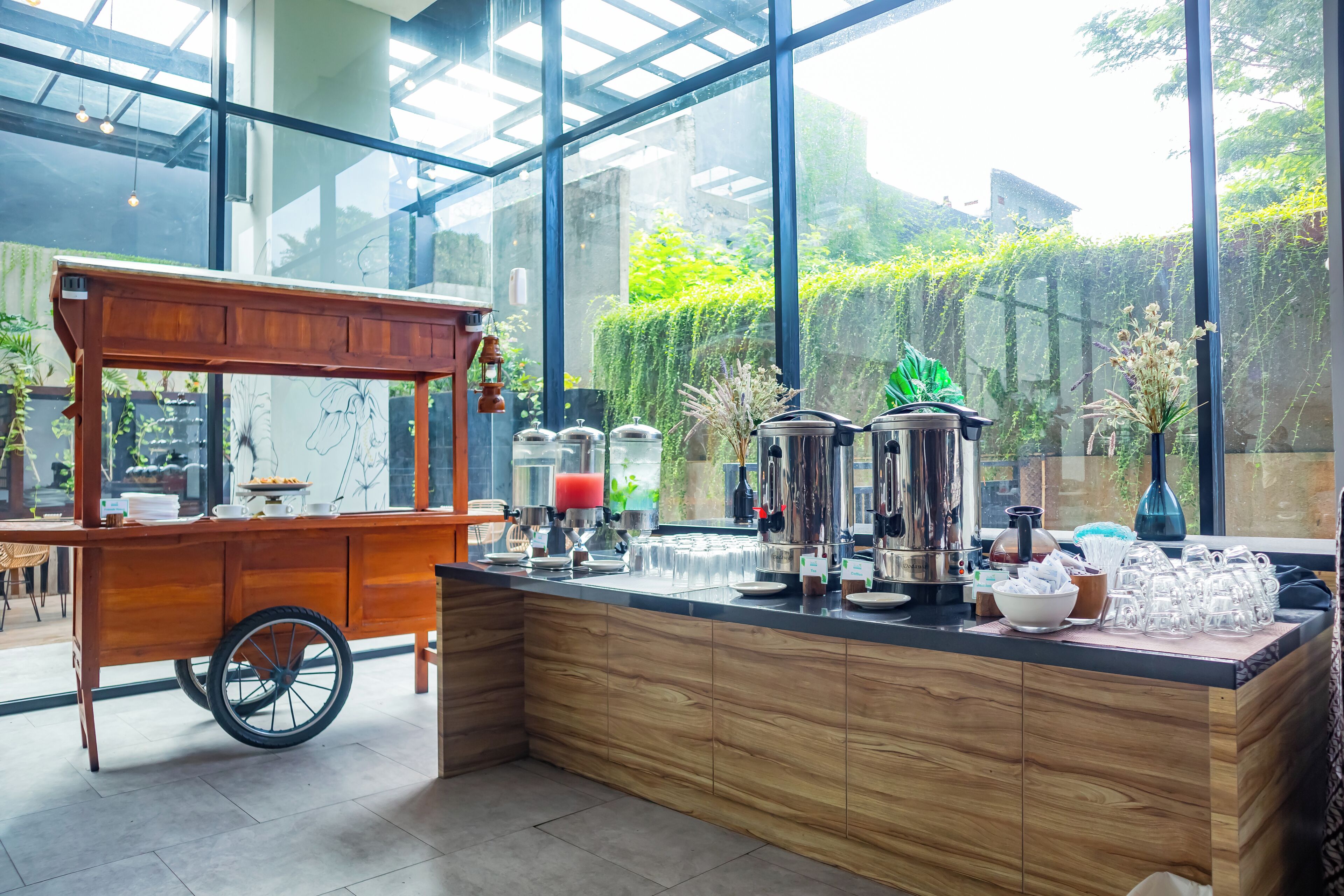 A coffee station with a cart, dispensers, and a variety of cups and glasses.