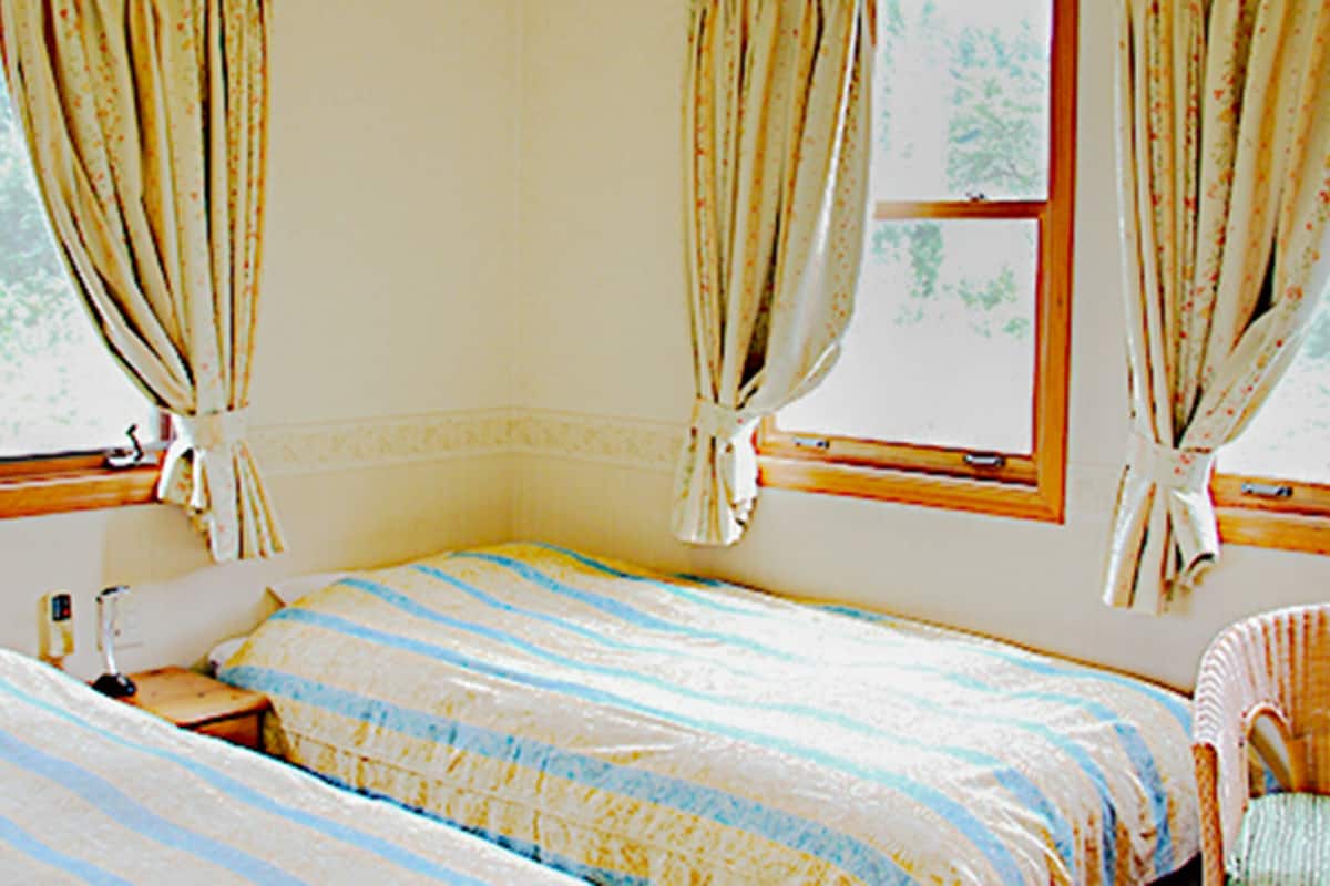 Un dormitorio con una cama, una silla y dos ventanas con cortinas.