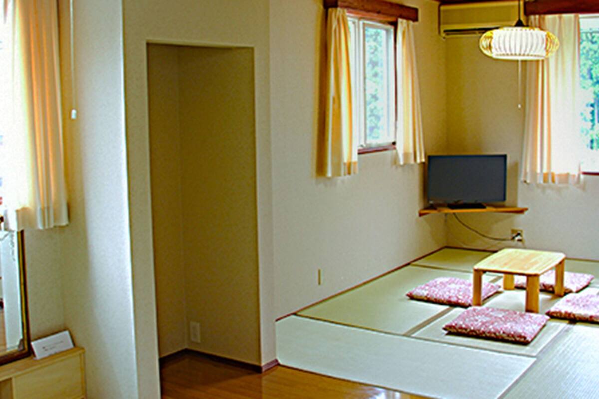 Una habitación con esteras de tatami, un televisor, una mesita y un espejo.