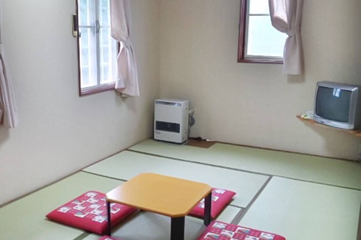 Una habitación con suelo de tatami, una mesita baja y un televisor sobre un mueble.