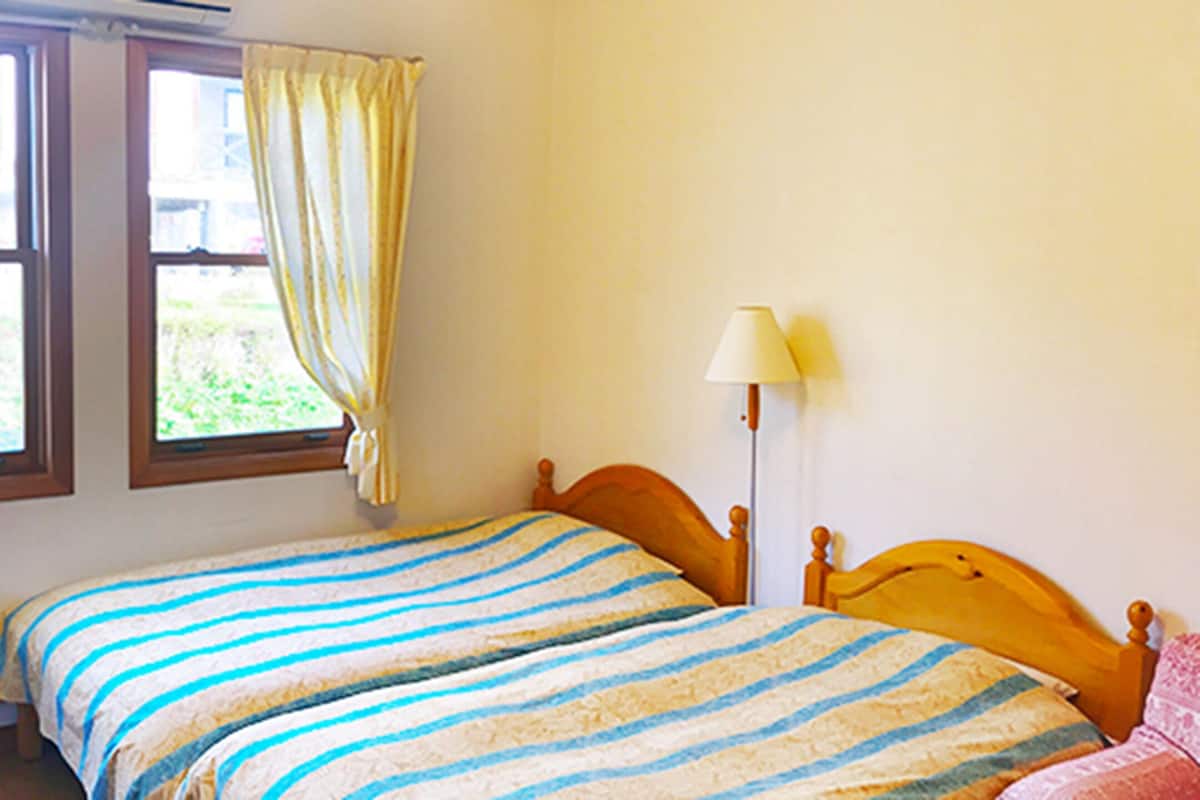 Un dormitorio con dos camas, una mesita de noche, una lámpara y una ventana con cortinas.