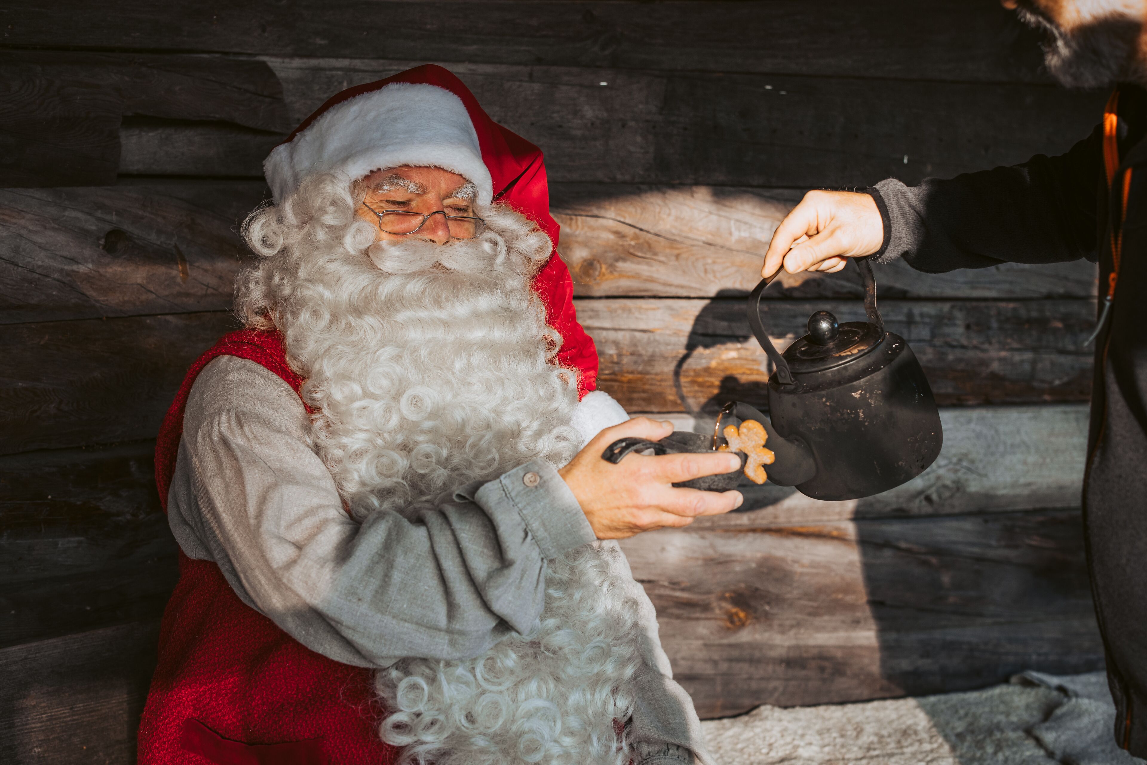 Une personne déguisée en Père Noël, tenant un pot noir doté d'une anse.