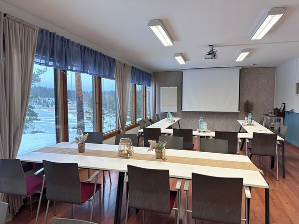 Una sala de conferencias con una larga mesa, sillas, una pantalla de proyector y grandes ventanas con vista nevada.