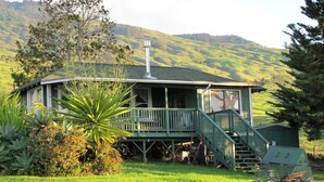 A green house with a porch and stairs, surrounded by lush greenery and hills. - Heaven on Earth in Upcountry Maui (Kula)