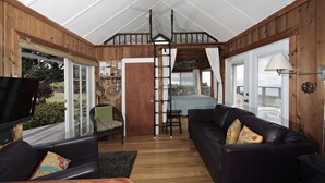 A cozy cabin interior with a wooden interior, a loft bedroom, a dining area, and a television. - Heaven on Earth in Upcountry Maui (Kula)