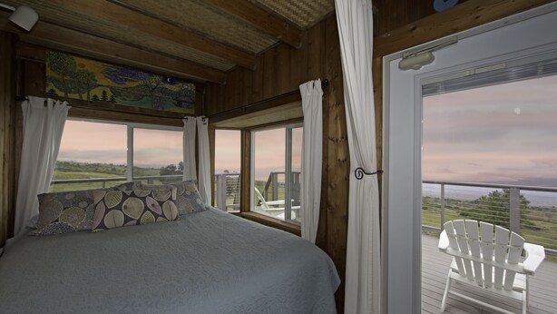 A bedroom with a large bed, a view of the outdoors, and a balcony with chairs. - Heaven on Earth in Upcountry Maui (Kula)