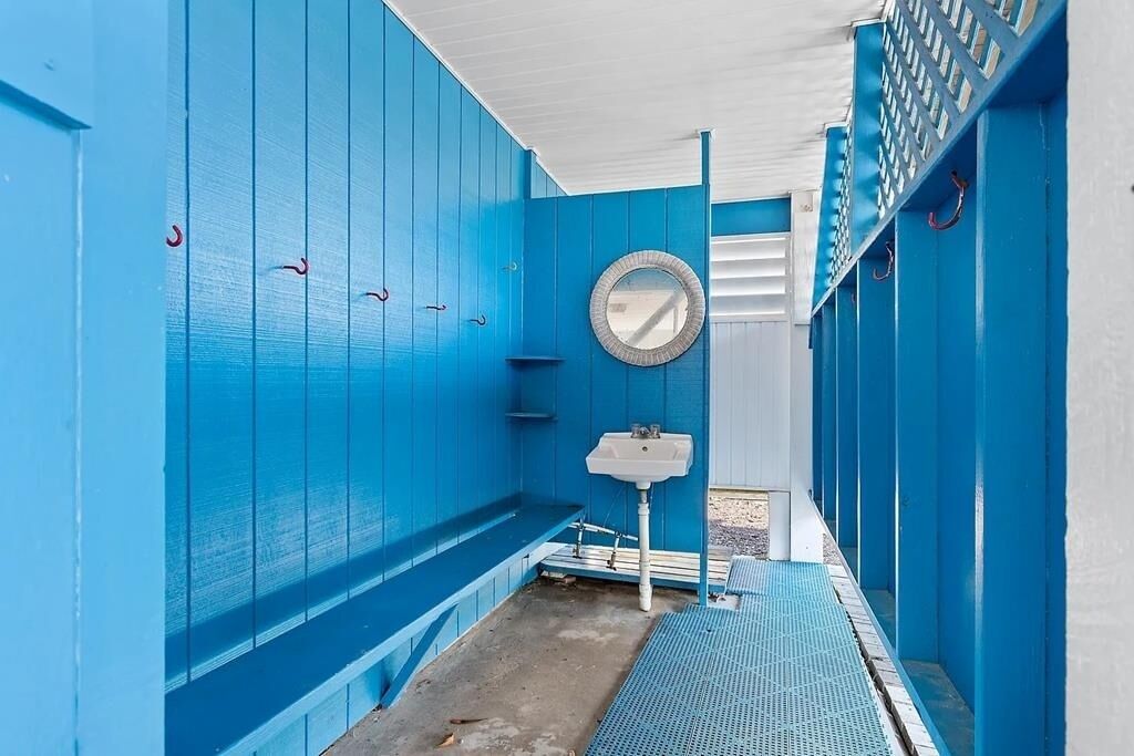 A narrow, blue-walled bathroom with a sink, mirror, and a small window.