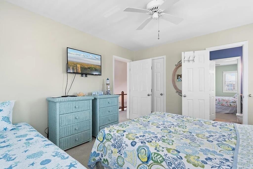 A bedroom with two beds, a ceiling fan, a dresser, and a television.