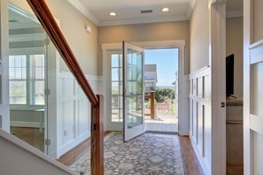 A hallway with a wooden staircase, a glass door leading outside, and a view of a backyard. - Absolute Paradise 5 Bedroom Home by RedAwning (Supply)