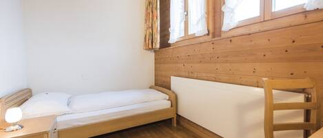 A single bed with a wooden headboard, a bedside table with a lamp, and a window with curtains.