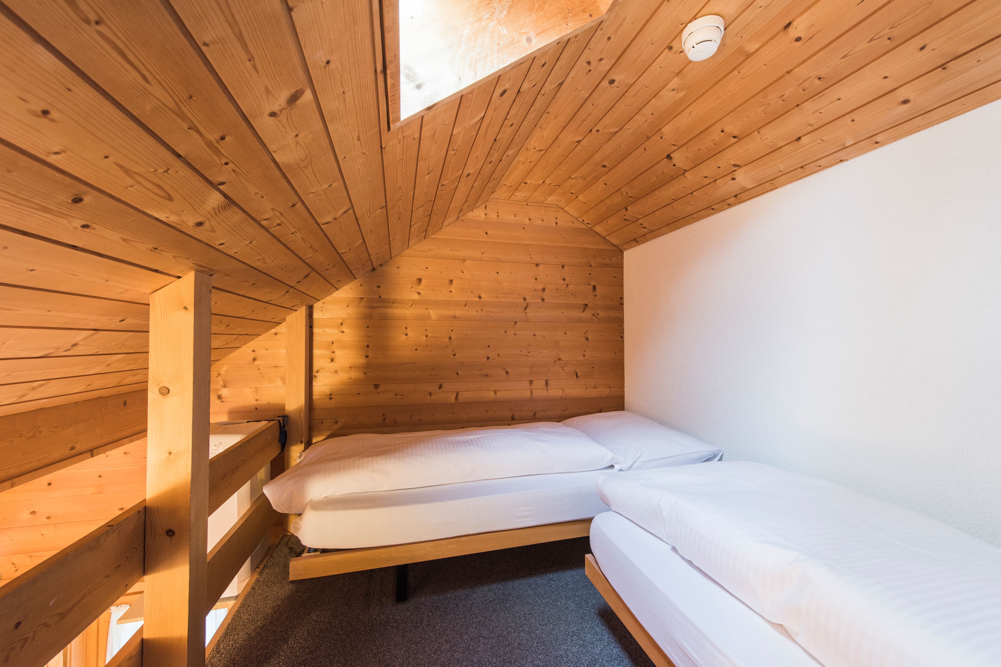 A small, wooden-paneled attic bedroom with two single beds and a skylight.