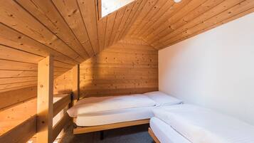 A small, wooden-paneled attic bedroom with two single beds and a skylight.
