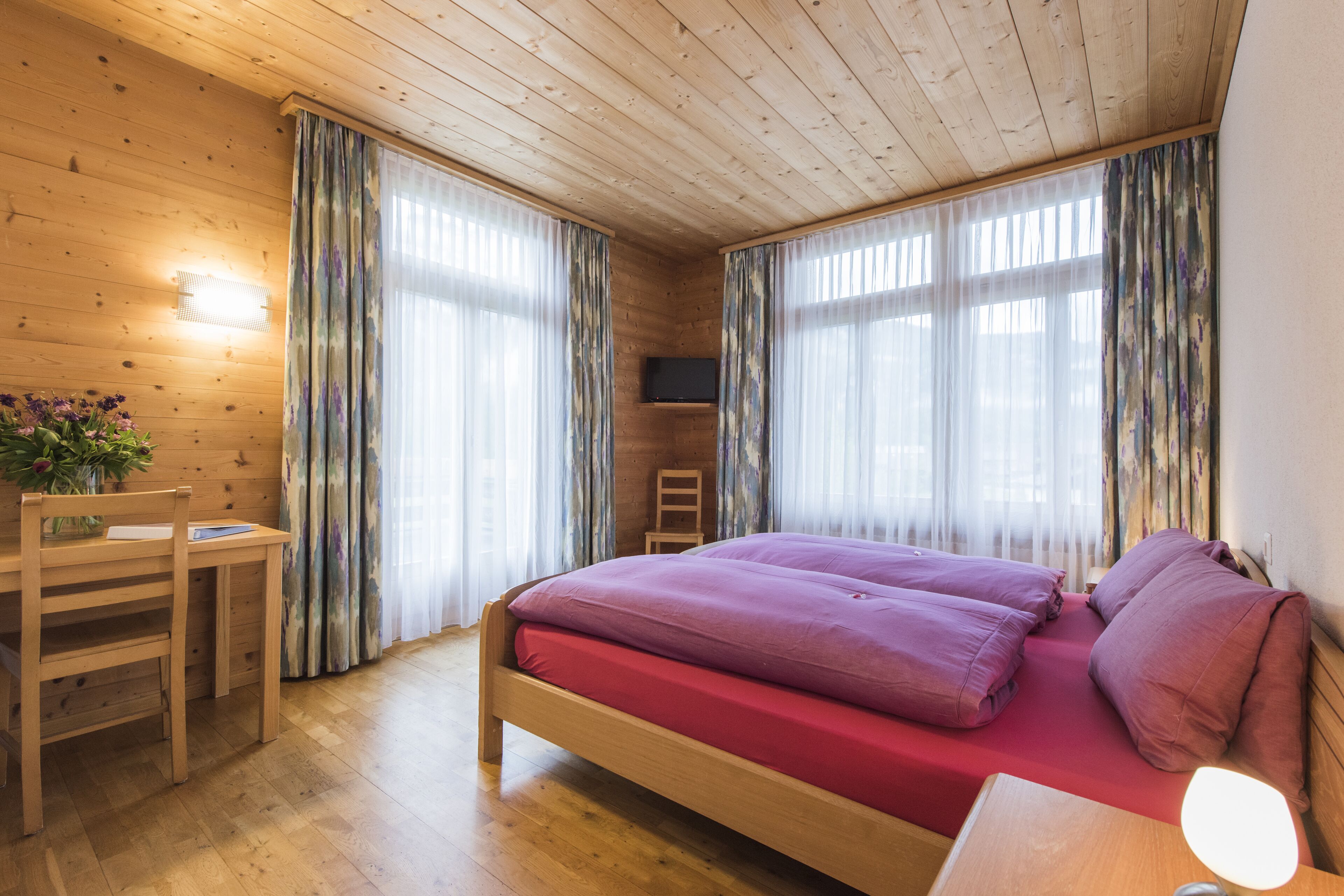 A wooden-paneled room with a bed, a desk, and a chair.