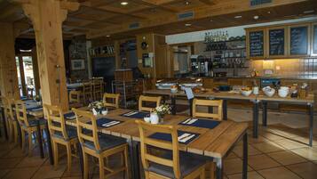 A restaurant with wooden tables and chairs, a bar area, and a menu board.