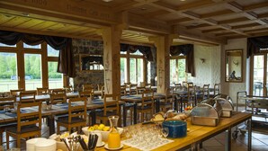 Comedor con varias mesas y sillas, un sistema de buffet y una pared de piedra con ventanas.