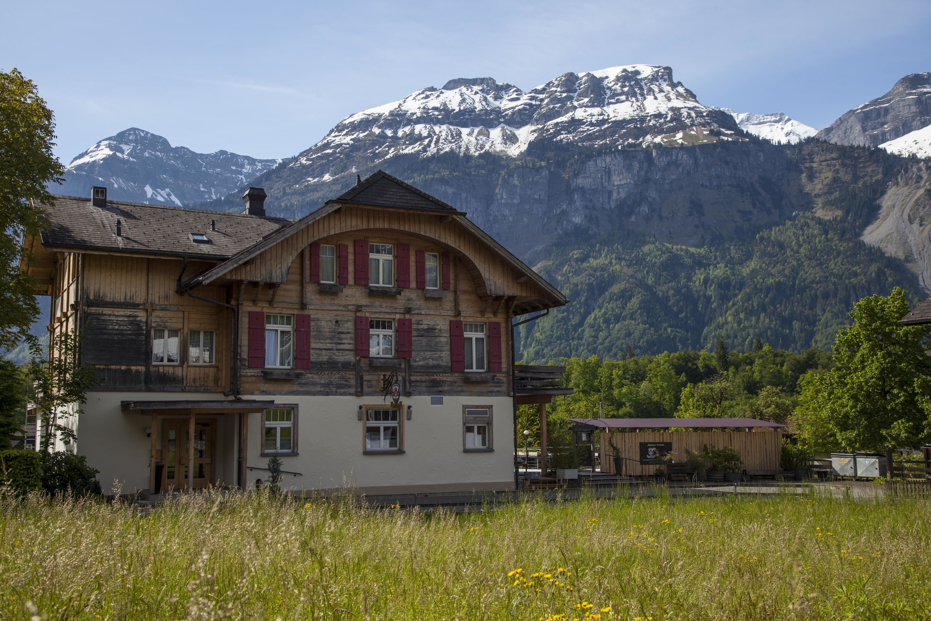 A wooden chalet with a balcony, set against a backdrop of snow-capped mountains.