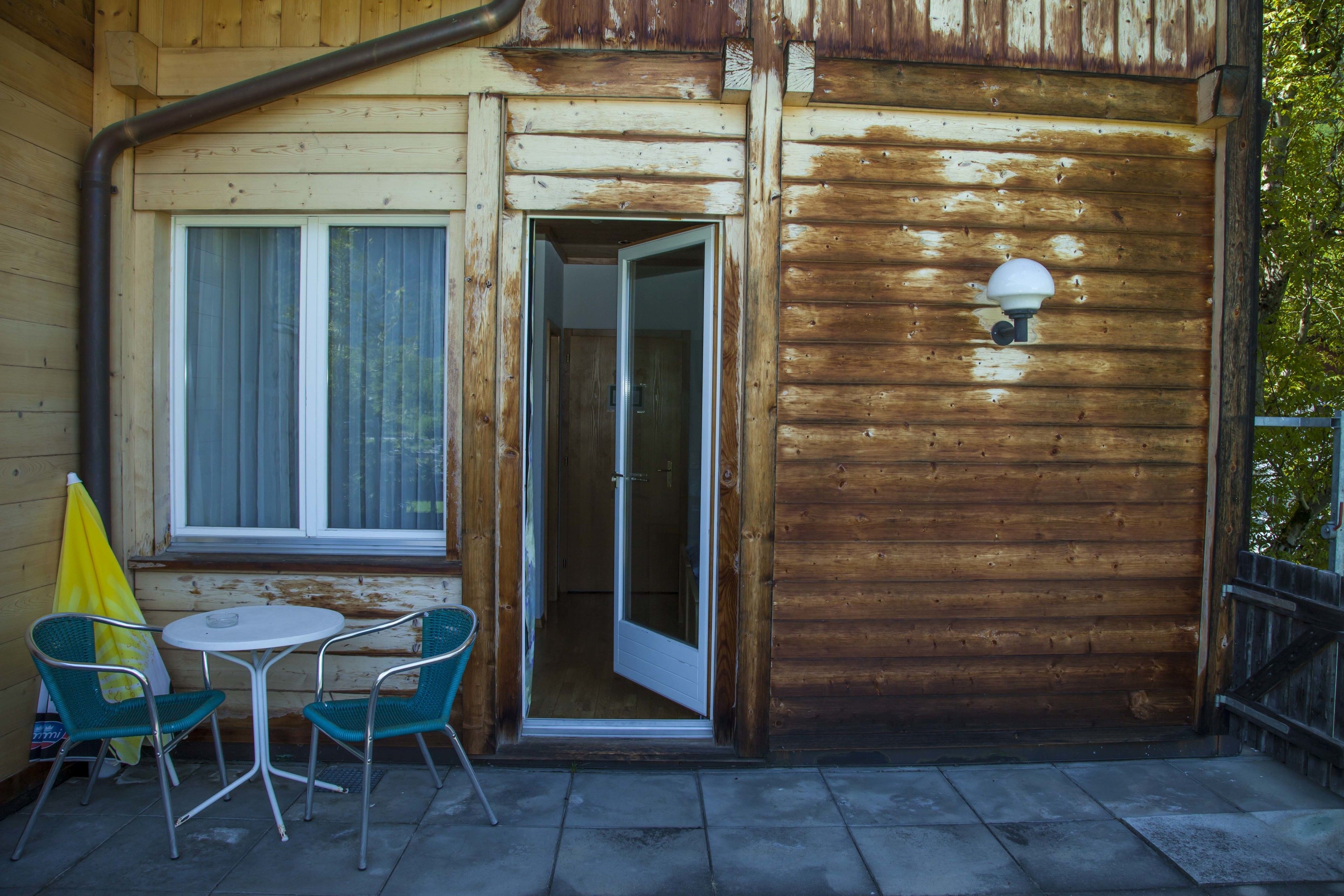 Una cabaña de madera con un pequeño patio, una puerta de acceso y una ventana con persianas.