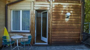Una cabaña de madera con un pequeño patio, una puerta de acceso y una ventana con persianas.