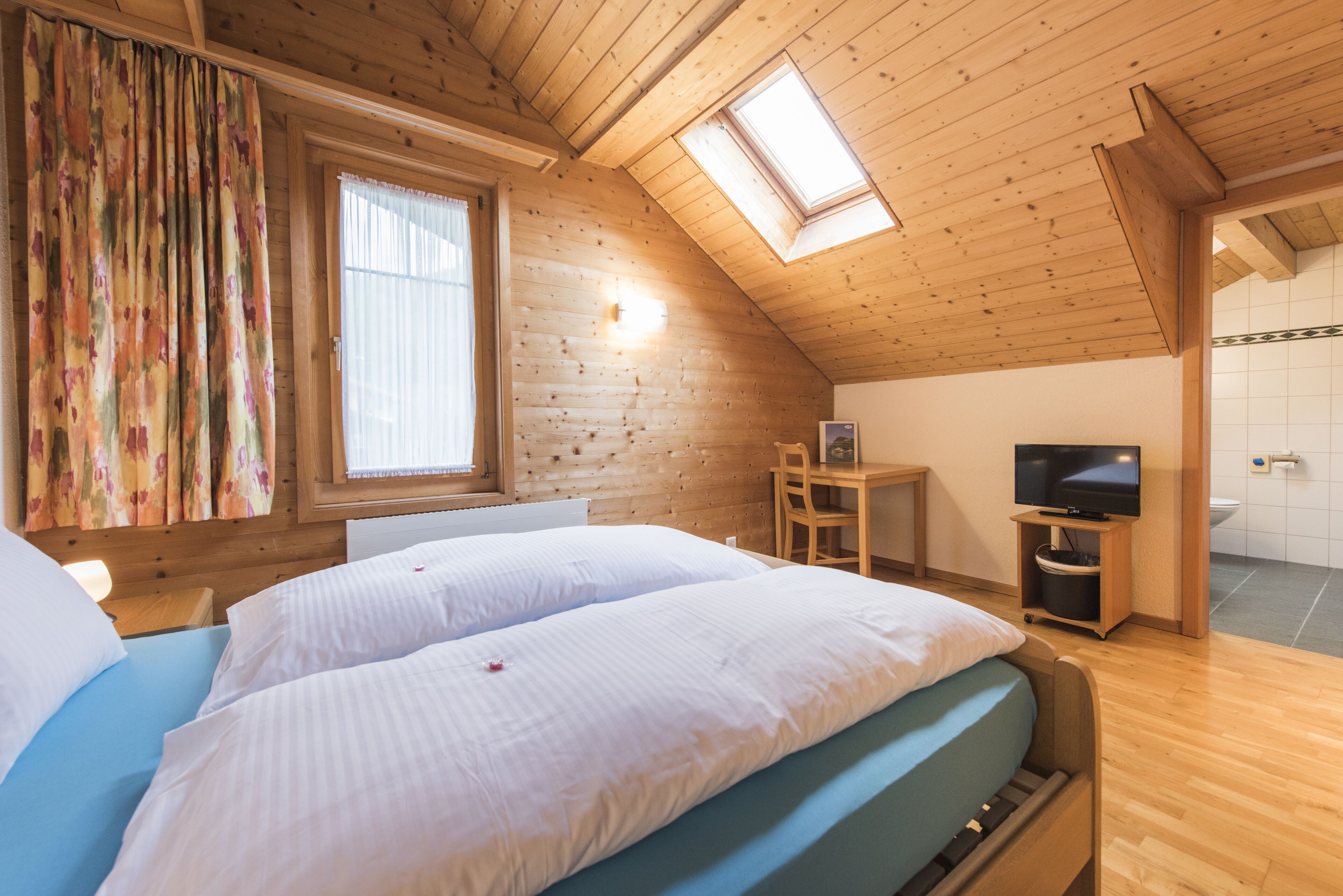 Une chambre avec deux lits, une télévision, un bureau et une fenêtre de toit.
