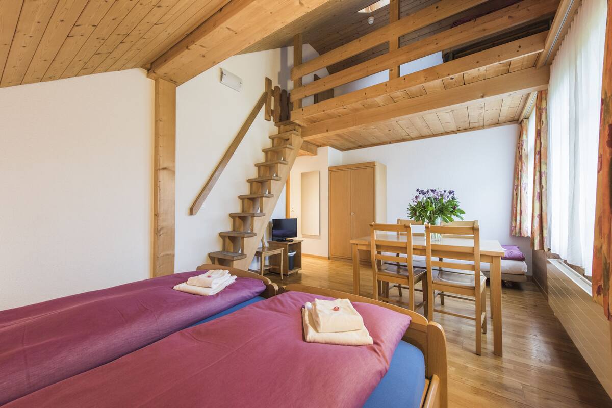 A room with two beds, wooden furniture, a staircase, and a television.