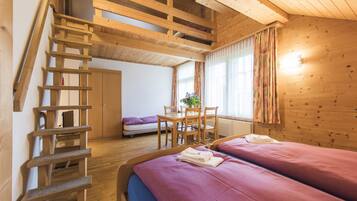 Un interior de madera con una escalera, dos camas con ropa de cama rosa, un comedor y un ventanal con cortinas.