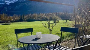 Un espacio de estar al aire libre con una mesa y sillas, con vista a un campo verde y montañas.