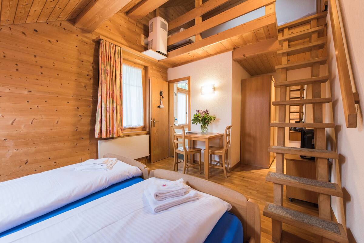 A wooden cabin room with two beds, a desk, and a chair.