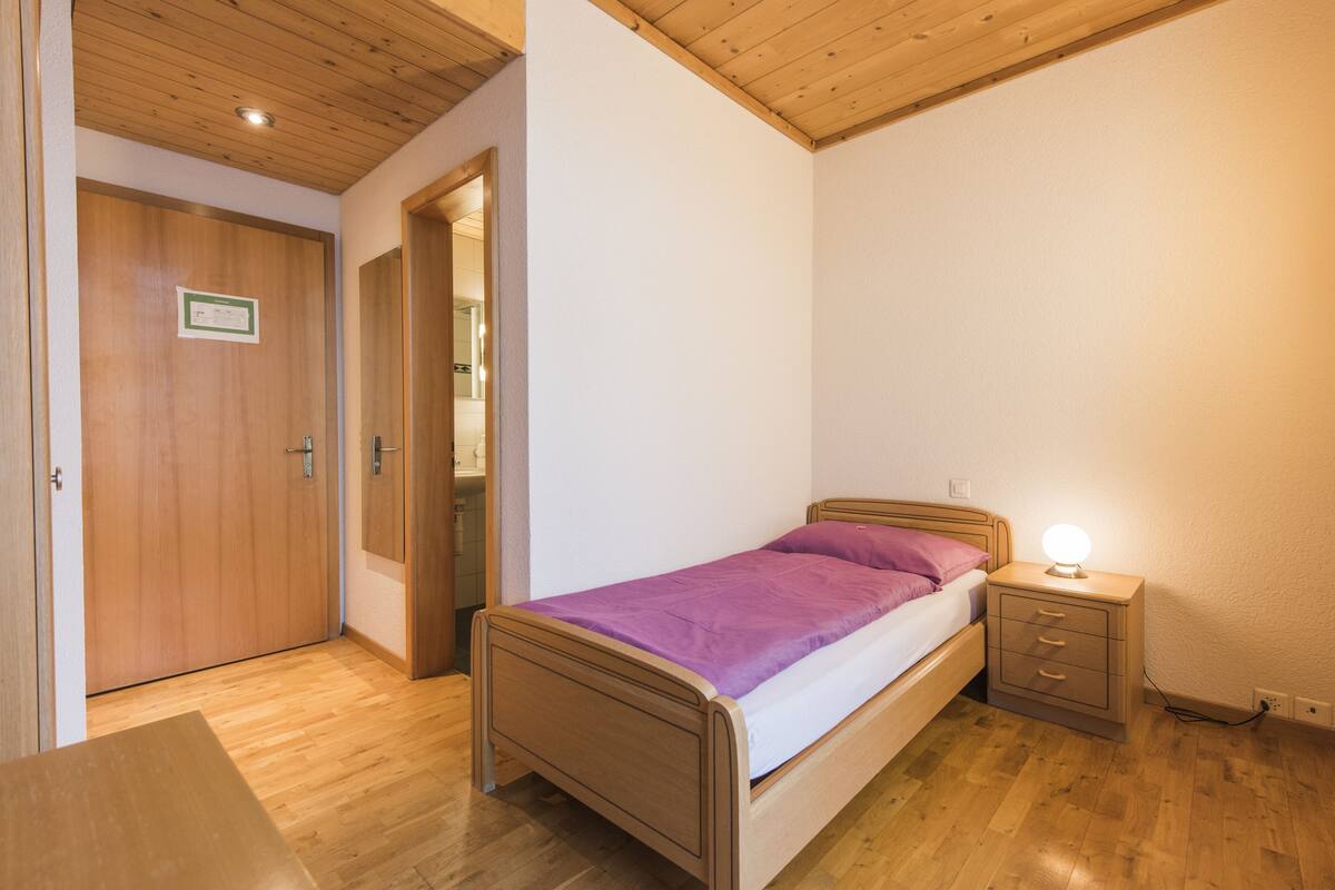 A bedroom with a wooden bed, a nightstand with a lamp, and a wooden door.
