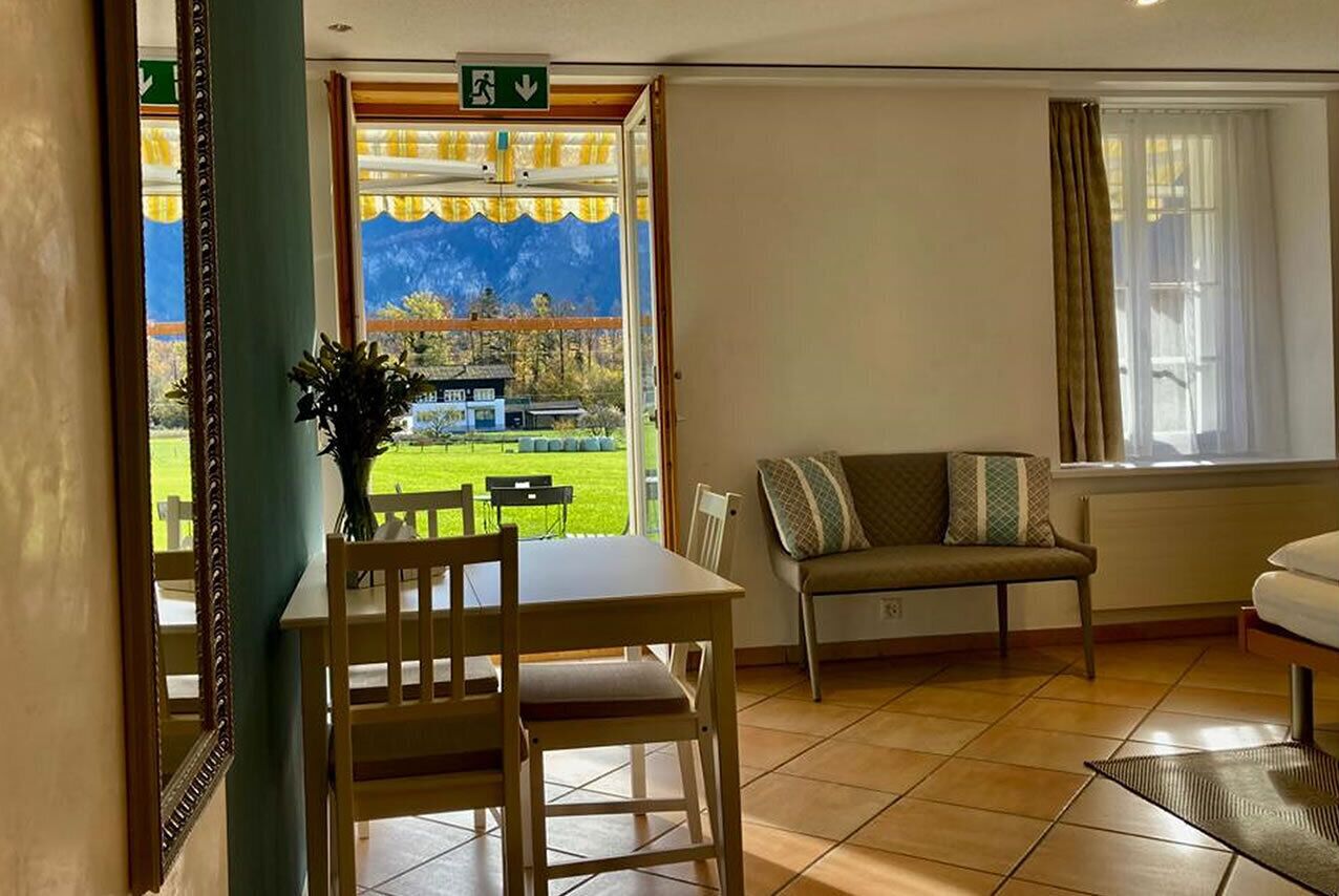 Una habitación con una mesa de comedor y sillas, un sofá y una ventana que ofrece vistas a un paisaje verde.