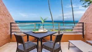 Un balcon avec une table et des chaises, donnant sur une plage et l’océan.
