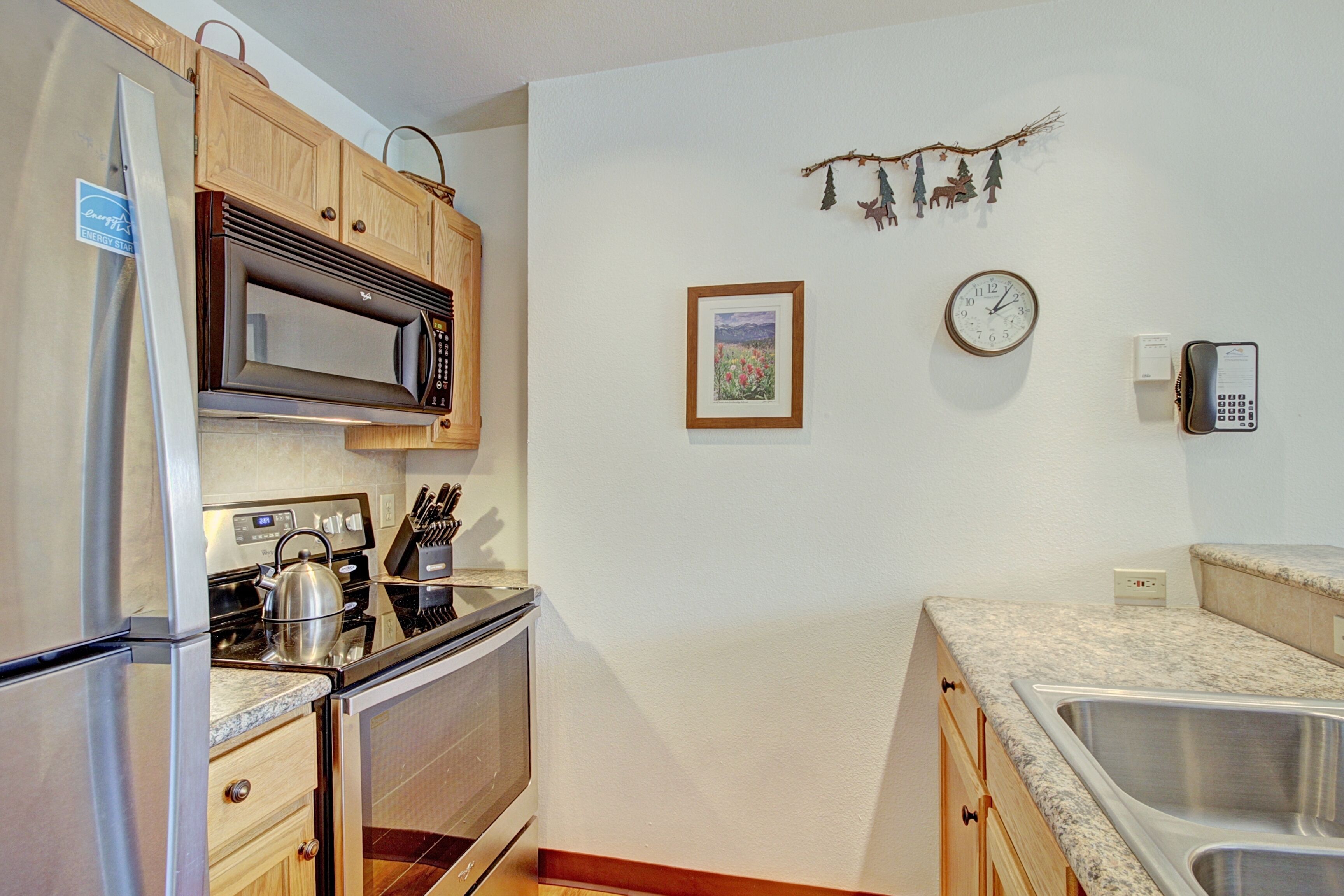 A kitchen with wooden cabinets, a stainless steel refrigerator, a microwave, a stove, and a sink.