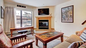 A living room with a fireplace, a television mounted above it, a large window with curtains, and a framed picture on the wall.