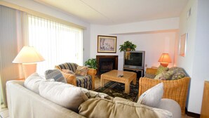 A living room with a sofa, two armchairs, a coffee table, a television, and a fireplace. - Crab Cove On The Bay 406 (Ocean City)